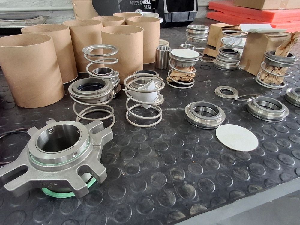 Sizwe Seals Springs - Mechanical Seal Repairs and Refurbishments Arrangement of mechanical seals, springs and industrial sealing components on a workshop table, representing industrial sealing solutions and maintenance
